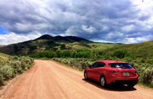 Photo of Red Mazda 3 iGrand Touring on dirt road with hills and cloudy sky ahead
